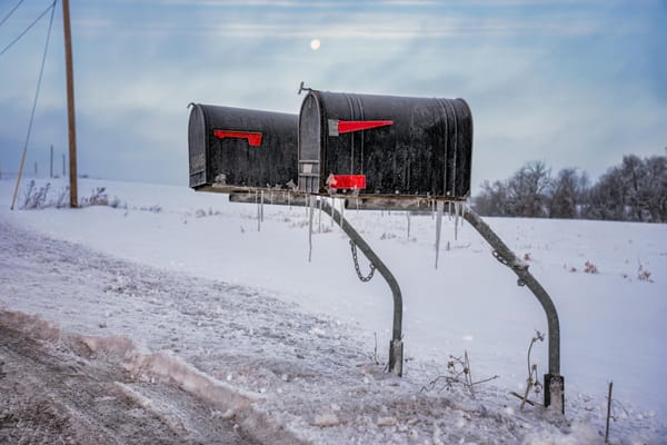 Two mailboxes with icicles in snow covered surroundings.